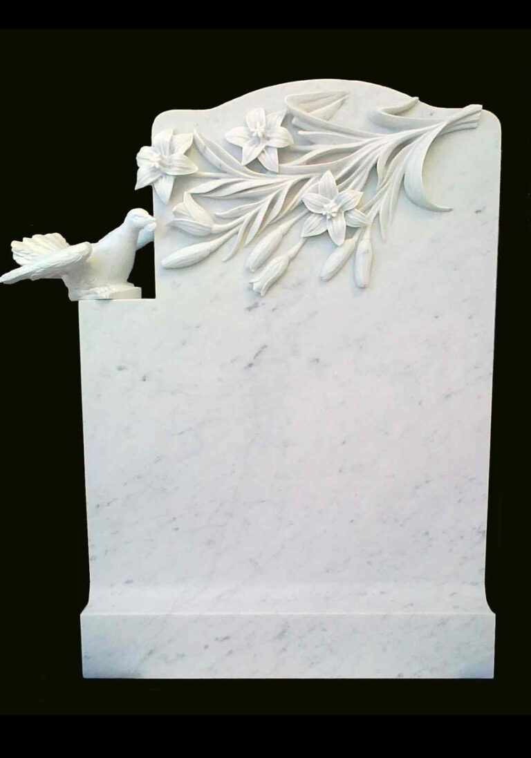 A white marble headstone with carved lilies and a perched bird, showcasing delicate floral details and a smooth finish against a black background.