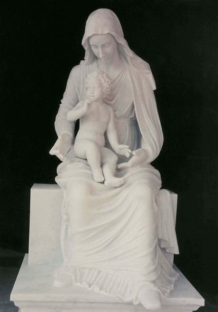 A white marble statue of the Virgin Mary seated, gently holding the infant Jesus on her lap, with intricate drapery and serene expressions, displayed against a black background.