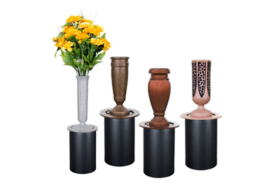 A selection of memorial vases in different styles and materials, including a gray vase with a cross design, a bronze vase, and a black polished vase, some adorned with fresh flowers.