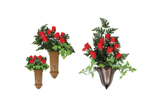 A collection of bronze wall-mounted vases filled with vibrant red roses and green foliage, designed for decorative or memorial purposes.